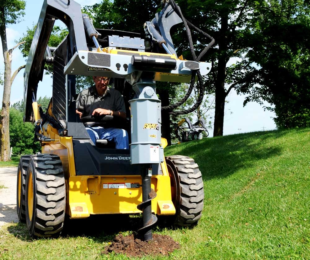 Skid steer auger drive and bits attachment drilling into soil for post hole installation